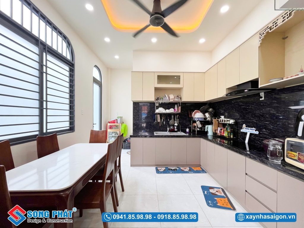 Không gian bếp chữ L hiện đại, tiện nghi kết hợp bàn ăn ấm cúng và hệ cửa sổ lớn đón sáng tự nhiên.