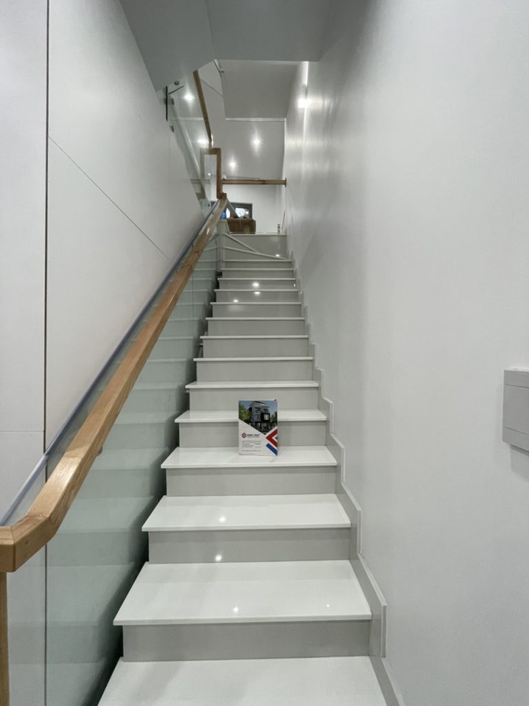 Cầu thang di chuyển lên các tầng được ốp đá trắng lan can kính cường lực tay vịn gỗ 