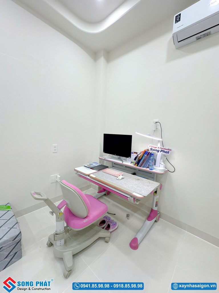 Góc phòng học tập với bàn ghế điều chỉnh độ cao màu hồng và máy tính để bàn gọn gàng.