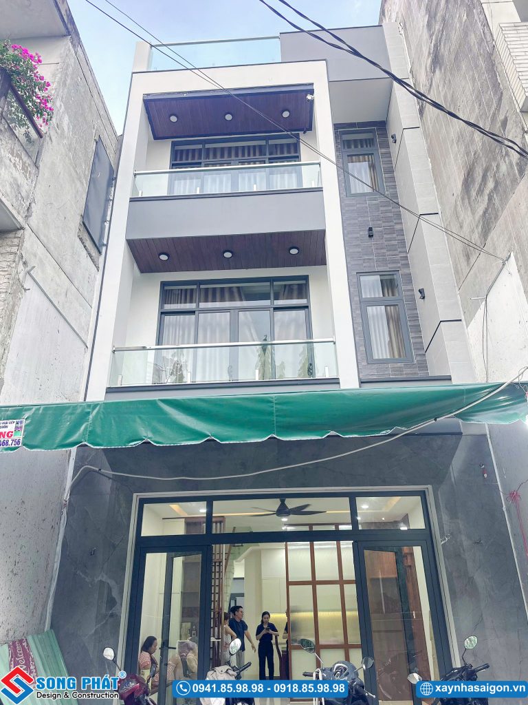 Tổng thể mặt tiền nhà phố nhiều tầng với hệ ban công kính, cửa khung nhôm xám và mảng tường ốp gạch điểm nhấn.