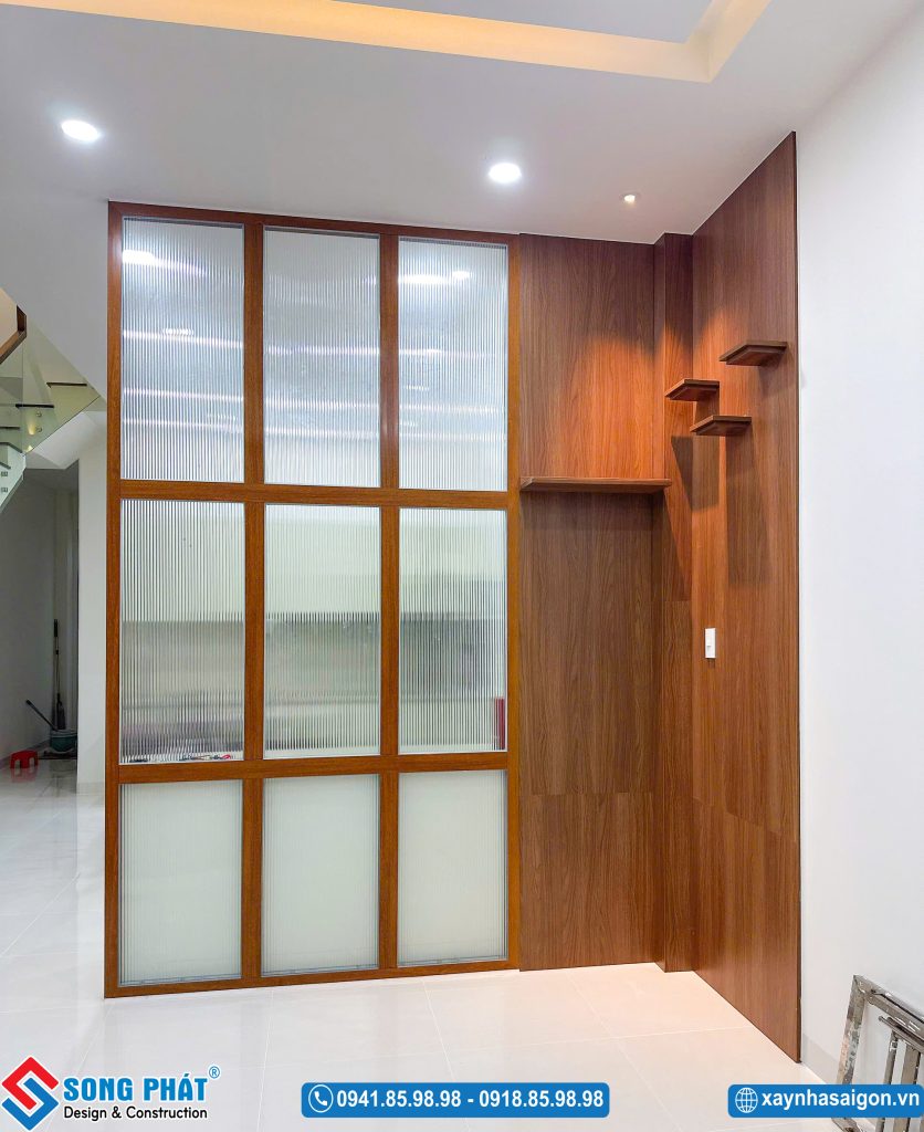 Vách ngăn kính sọc kết hợp hệ ốp tường gỗ và các kệ trang trí nhỏ gọn tại tầng trệt.