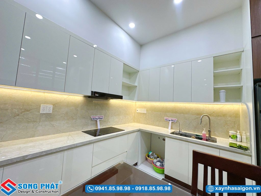 Không gian nấu nướng với hệ tủ bếp trên dưới màu trắng sáng, mặt đá vân mây và bồn rửa tiện lợi.