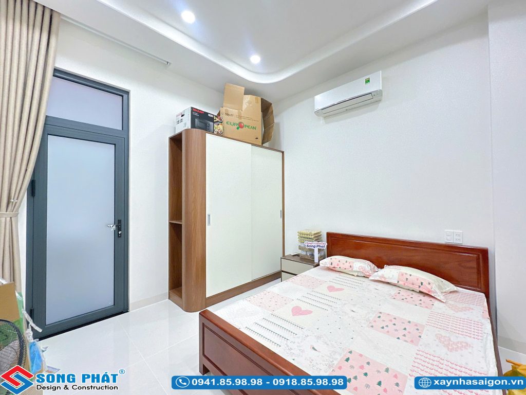 Không gian phòng ngủ thông thoáng với giường gỗ, tủ quần áo cửa lùa và điều hòa.