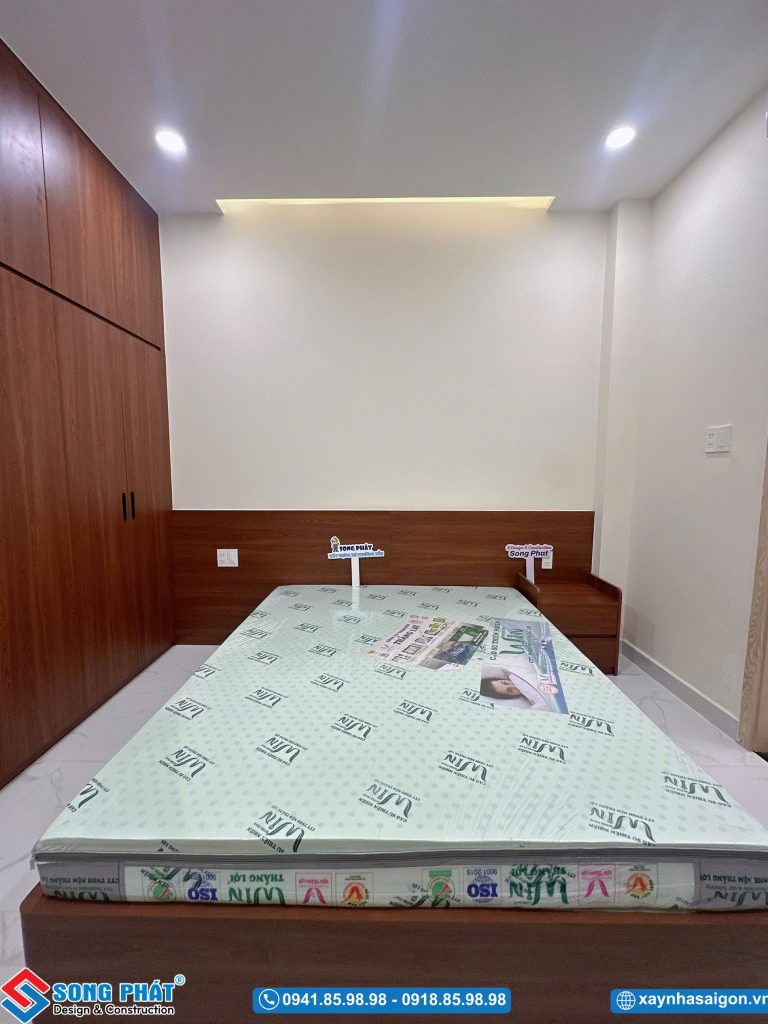 Tổng quan khu vực giường ngủ bố trí sát tường với hệ đèn trần chiếu sáng tinh tế.