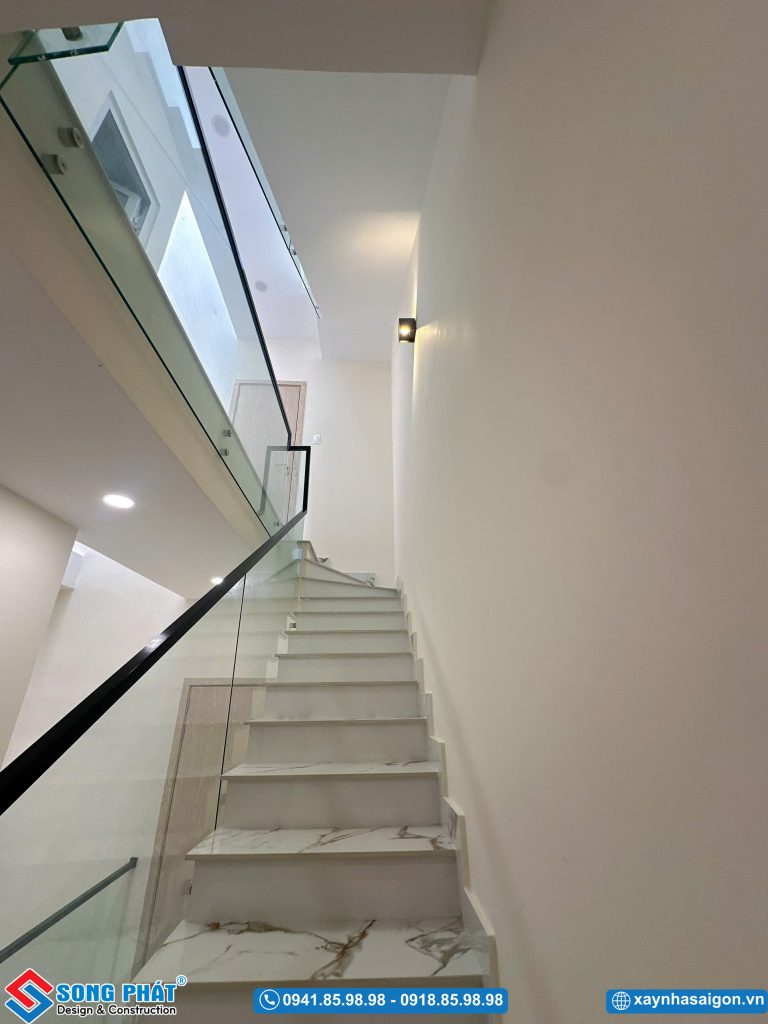 Cầu thang lát đá trắng vân mây kết hợp lanຄan kính và đèn hắt tường trang nhã.
