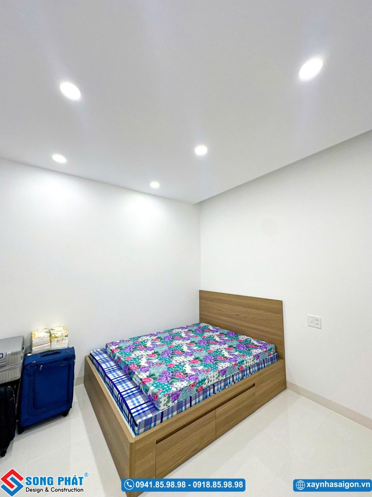 Phòng ngủ nhỏ gọn giản dị với giường gỗ và chăn ga gối nệm họa tiết hoa.