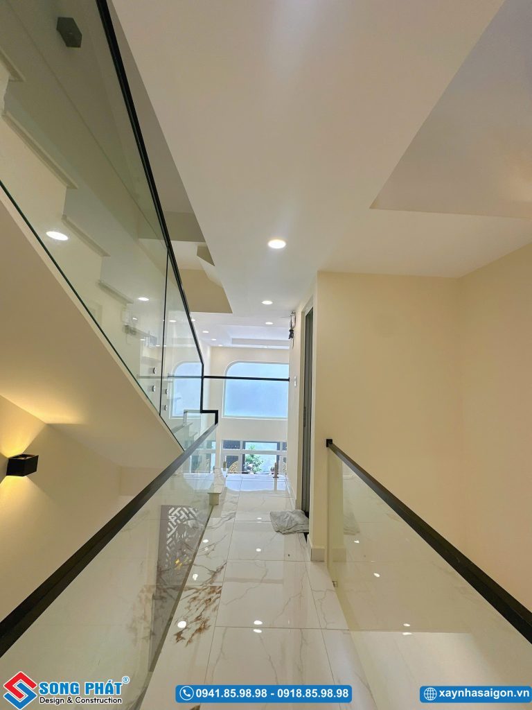 Lối đi hành lang lầu trên với lan can kính và hệ thống đèn hắt tường trang nhã.
