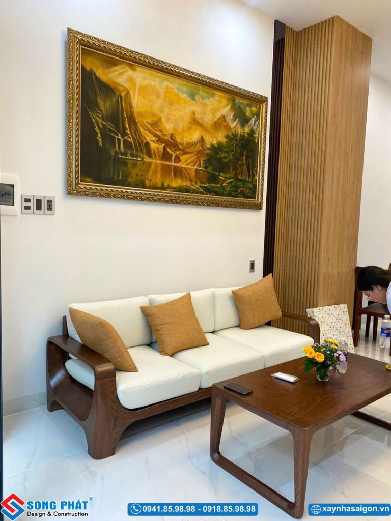 Không gian tiếp khách bố trí bộ sofa gỗ, tranh treo tường và đèn chùm.