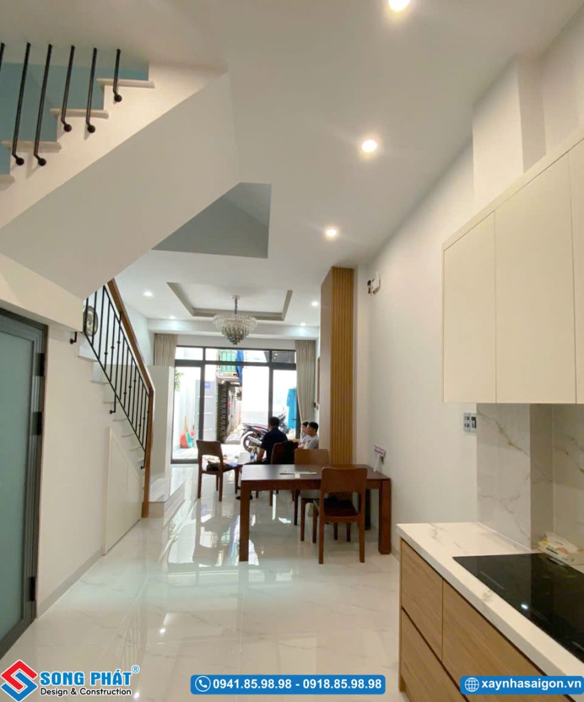 Góc nhìn từ khu vực bếp hướng ra cửa chính qua bộ bàn ăn và phòng khách.