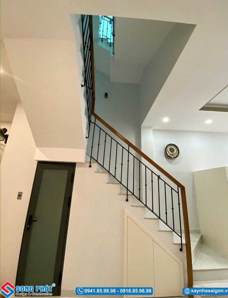Cầu thang bộ kết hợp lan can sắt nghệ thuật, tay vịn gỗ và tủ lưu trữ tận dụng gầm cầu thang.