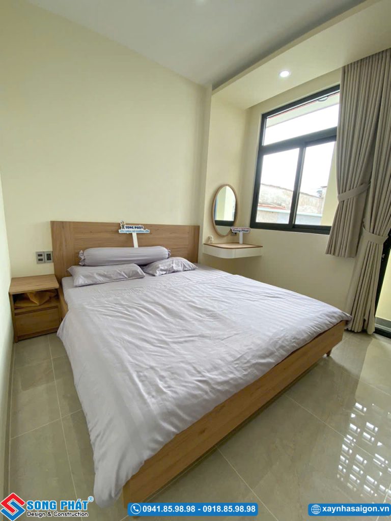 Căn phòng ngủ đơn giản, ấm cúng với giường gỗ và bàn trang điểm treo tường cạnh cửa sổ.