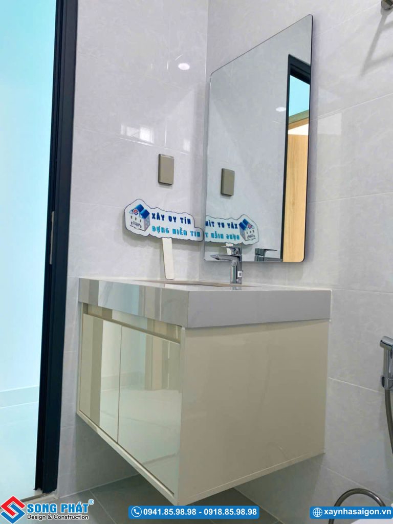 Khu vực chậu rửa mặt với tủ lavabo treo tường màu kem và gương soi cỡ lớn.