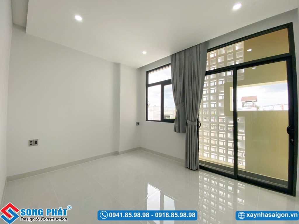 Không gian phòng ngủ trống thoáng đãng với cửa kính lớn ra ban công và cửa sổ lấy sáng.